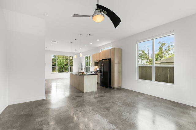 kitchen featuring fridge with ice dispenser, hanging light fixtures, a center island with sink, and concrete floors