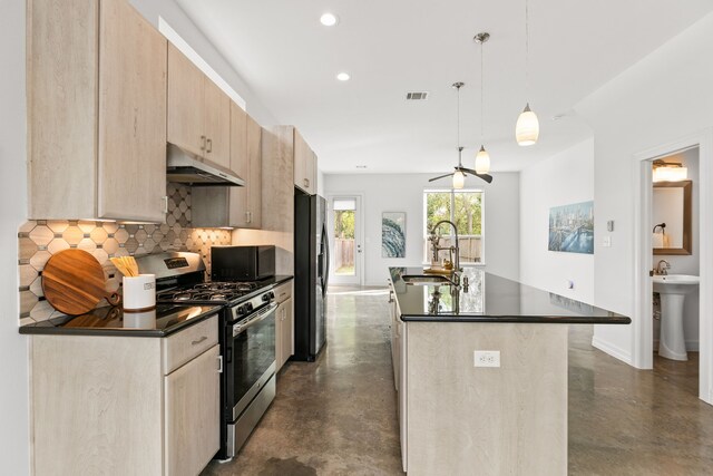 kitchen featuring a center island with sink, stainless steel appliances, decorative light fixtures, light brown cabinetry, and sink