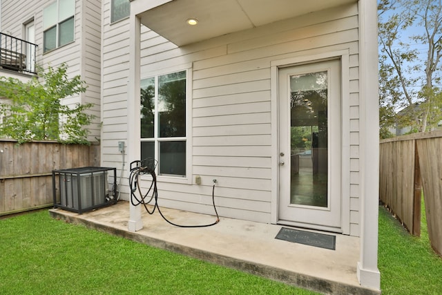 view of exterior entry featuring a balcony, a lawn, central AC, and a patio