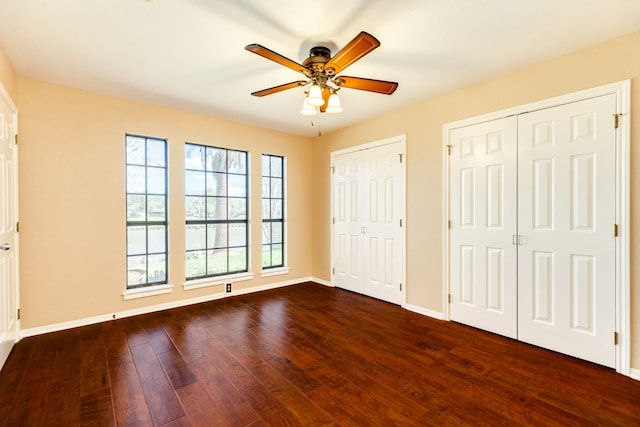 unfurnished bedroom with two closets, dark hardwood / wood-style floors, and ceiling fan