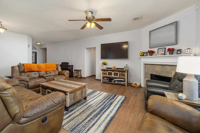 living room with a tile fireplace, hardwood / wood-style flooring, and ceiling fan