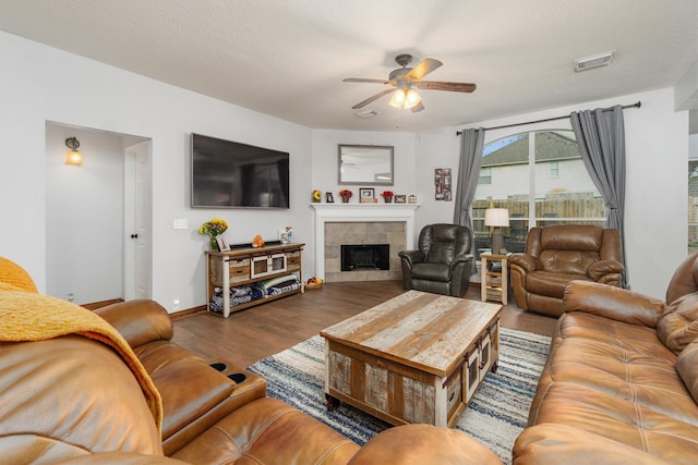 living room featuring wood-type flooring, a tile fireplace, ceiling fan, and a textured ceiling