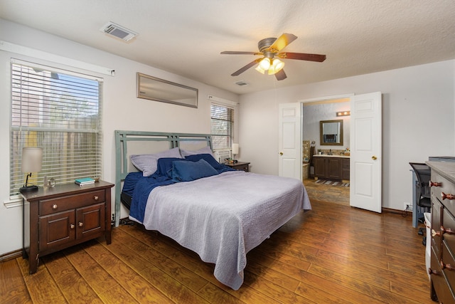 bedroom with ceiling fan, connected bathroom, a textured ceiling, and dark hardwood / wood-style flooring