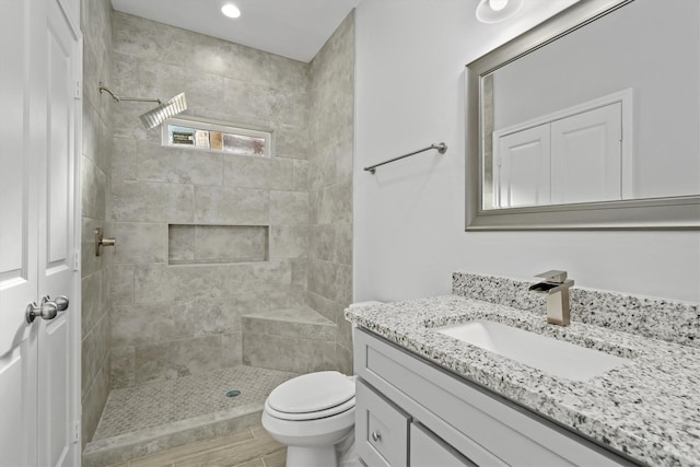 bathroom featuring vanity, toilet, wood-type flooring, and tiled shower