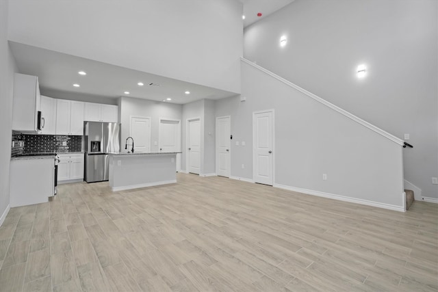 unfurnished living room featuring sink, a high ceiling, and light hardwood / wood-style flooring