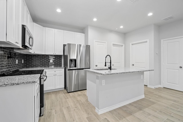 kitchen featuring light stone countertops, white cabinetry, a center island with sink, and stainless steel appliances