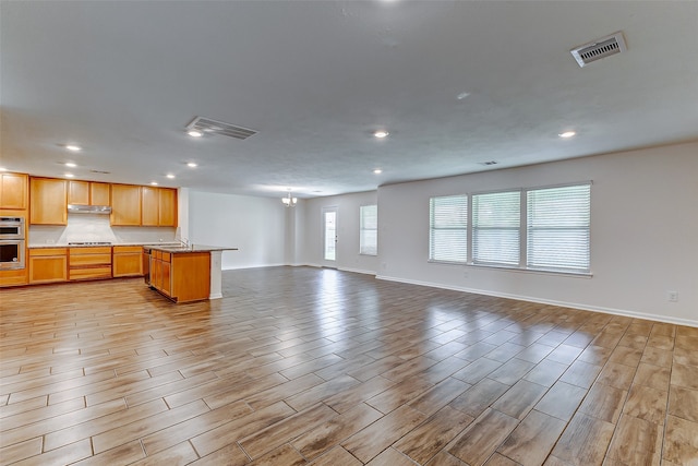 kitchen with cooktop, sink, an island with sink, stainless steel double oven, and light wood-type flooring