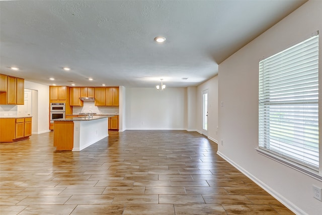 kitchen featuring sink, an inviting chandelier, light hardwood / wood-style floors, double oven, and a kitchen island with sink