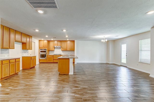 kitchen with an inviting chandelier, sink, a kitchen island with sink, double oven, and decorative light fixtures