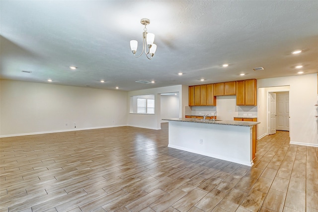 kitchen featuring dark stone countertops, light wood-type flooring, an inviting chandelier, and a center island with sink