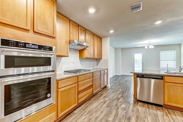 kitchen featuring a textured ceiling, a chandelier, light stone countertops, light wood-type flooring, and appliances with stainless steel finishes