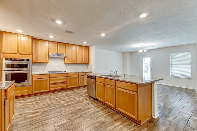 kitchen featuring stainless steel appliances, a center island with sink, sink, a textured ceiling, and light wood-type flooring