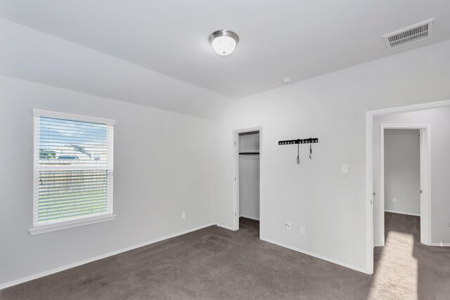 unfurnished bedroom featuring a closet, lofted ceiling, and dark colored carpet