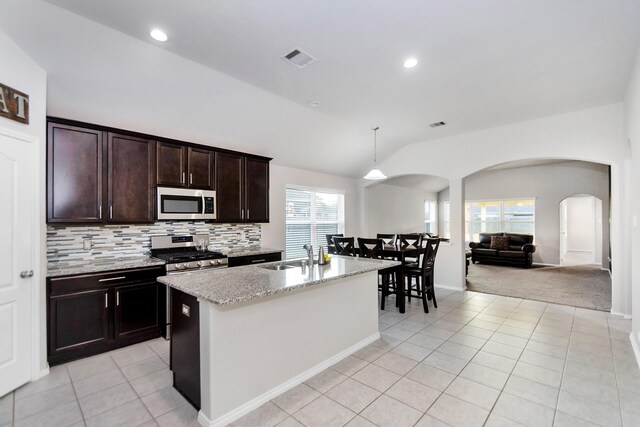 kitchen featuring sink, appliances with stainless steel finishes, decorative light fixtures, a kitchen island with sink, and lofted ceiling