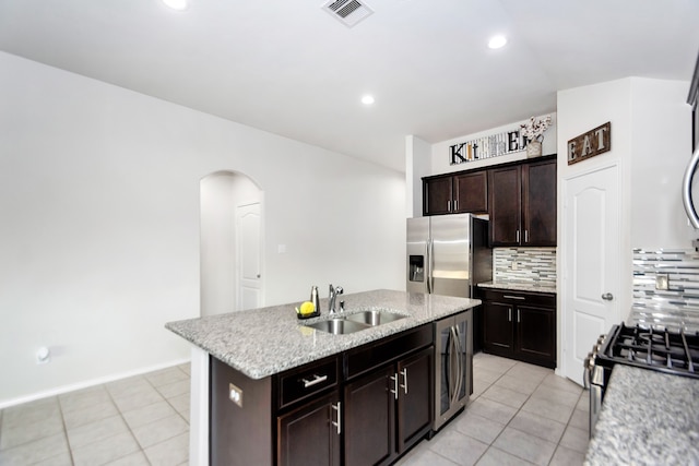 kitchen featuring dark brown cabinetry, sink, tasteful backsplash, a kitchen island with sink, and appliances with stainless steel finishes