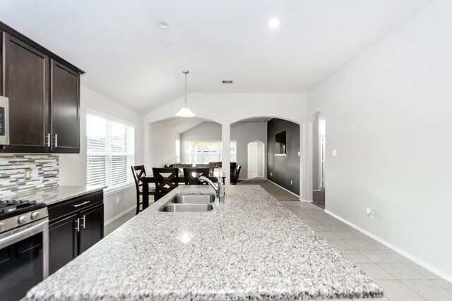 kitchen with stainless steel gas stove, lofted ceiling, sink, and light stone counters