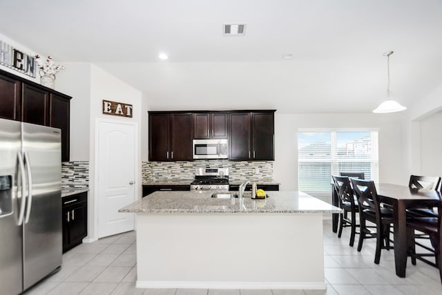 kitchen with stainless steel appliances, a center island with sink, pendant lighting, and light stone counters