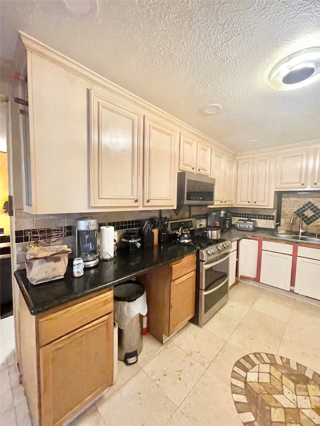 kitchen featuring stainless steel appliances, sink, tasteful backsplash, a textured ceiling, and light tile patterned floors