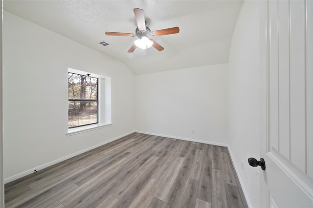 unfurnished room with a textured ceiling, light hardwood / wood-style flooring, and vaulted ceiling