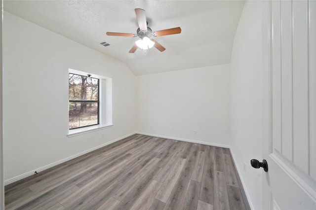 empty room with baseboards, wood finished floors, and vaulted ceiling