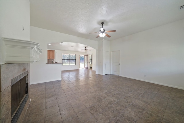 unfurnished living room with a tiled fireplace, baseboards, a ceiling fan, and arched walkways