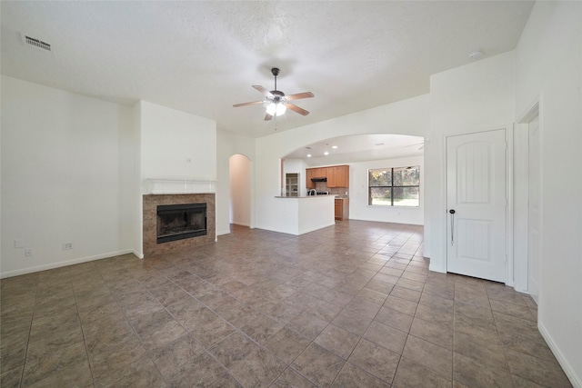 unfurnished living room with ceiling fan, a fireplace, arched walkways, visible vents, and baseboards