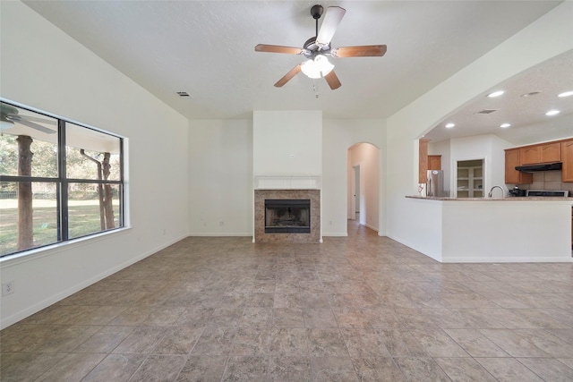 unfurnished living room featuring baseboards, a ceiling fan, visible vents, arched walkways, and a tile fireplace