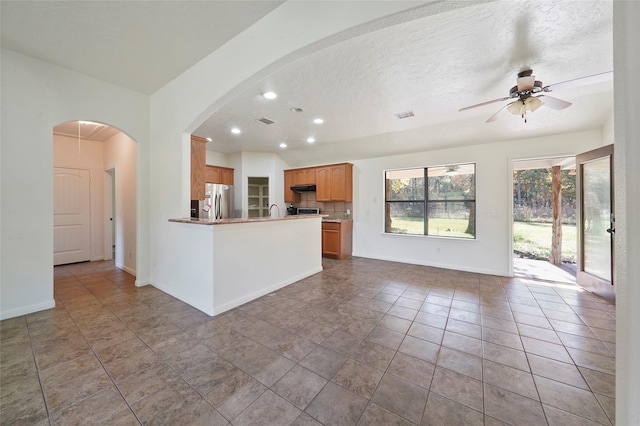 kitchen with open floor plan, a peninsula, a ceiling fan, freestanding refrigerator, and backsplash