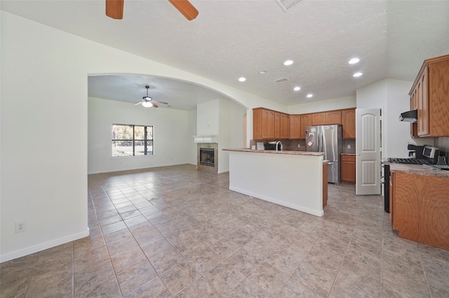 kitchen featuring sink, range hood, a textured ceiling, a tiled fireplace, and appliances with stainless steel finishes