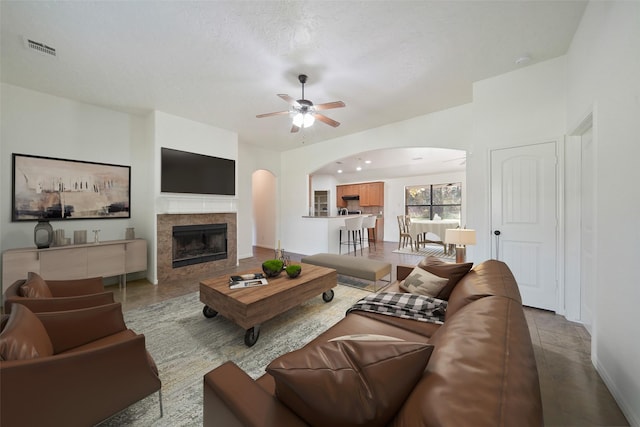 living room featuring arched walkways, a tile fireplace, visible vents, and ceiling fan