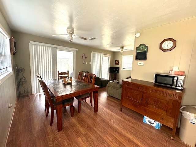 dining area featuring a textured ceiling, wood walls, hardwood / wood-style flooring, and ceiling fan