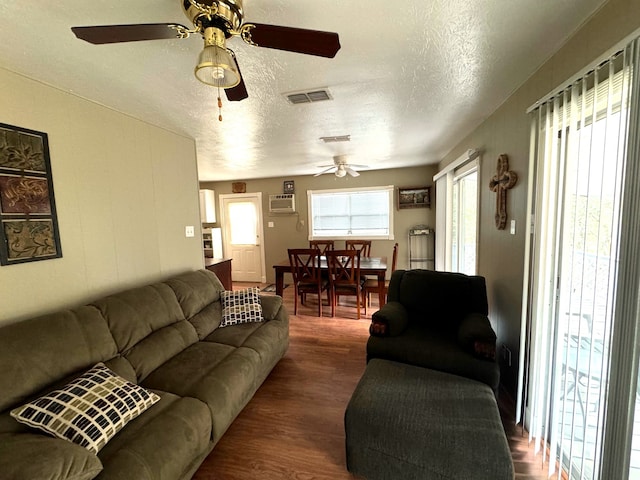 living room with dark wood-type flooring, ceiling fan, a textured ceiling, and an AC wall unit