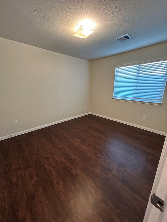 spare room featuring a textured ceiling and dark hardwood / wood-style flooring