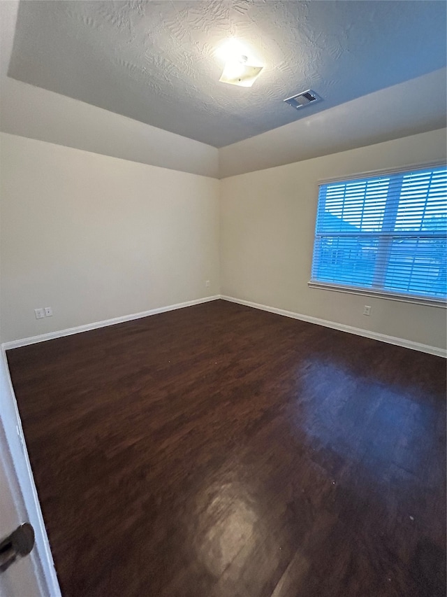 empty room featuring a textured ceiling and dark hardwood / wood-style floors