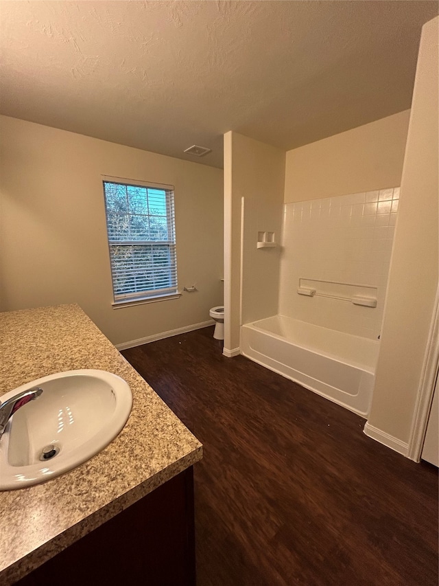 full bathroom with toilet, hardwood / wood-style floors, a textured ceiling, vanity, and tub / shower combination