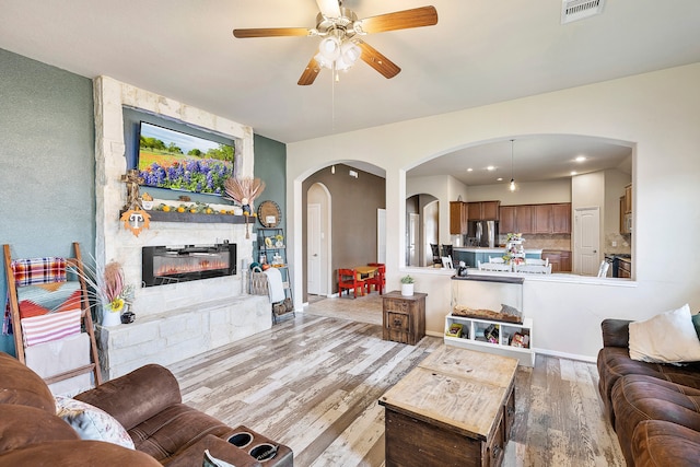 living room featuring a stone fireplace, light hardwood / wood-style floors, and ceiling fan