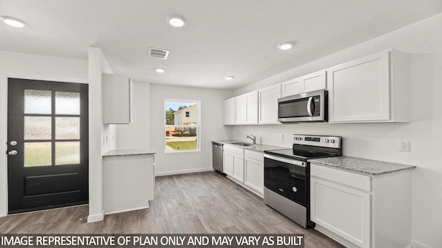 kitchen featuring white cabinets, light stone countertops, light hardwood / wood-style flooring, and appliances with stainless steel finishes