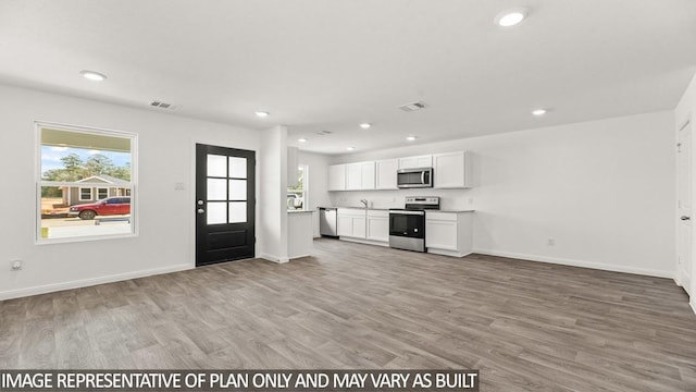 11938 Midas Ln, Willis, TX 77378 - kitchen featuring stainless steel appliances, open floor plan, white cabinets, light wood finished floors, and recessed lighting