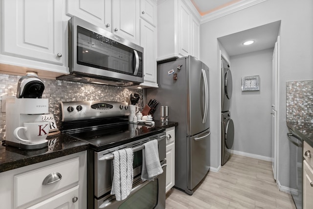 kitchen with light hardwood / wood-style flooring, stacked washer / dryer, backsplash, white cabinetry, and appliances with stainless steel finishes