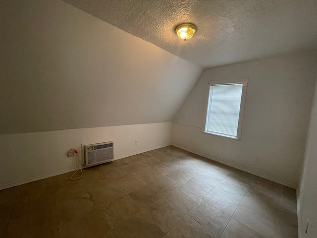 additional living space featuring an AC wall unit, lofted ceiling, and a textured ceiling