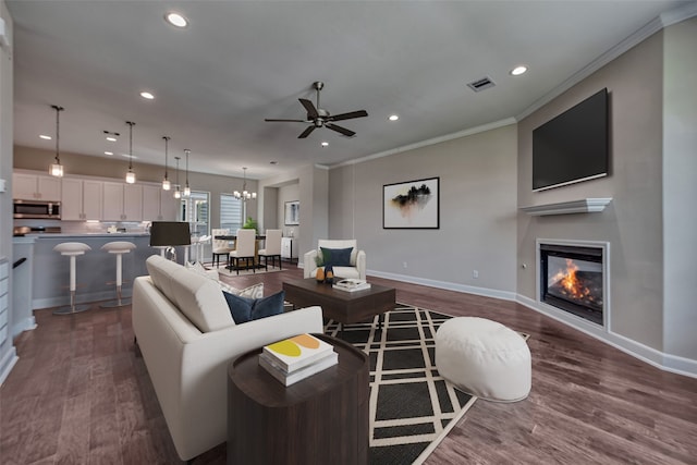 living room featuring dark wood-type flooring, ceiling fan with notable chandelier, and crown molding