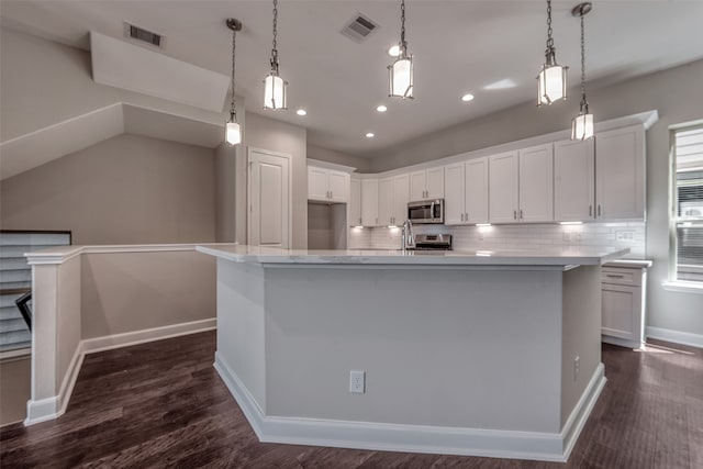 kitchen with an island with sink, white cabinetry, dark wood-type flooring, and backsplash