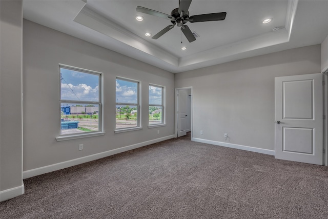 spare room with a tray ceiling, dark colored carpet, and ceiling fan