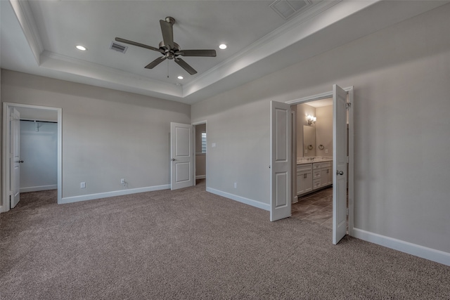 unfurnished bedroom featuring ensuite bathroom, ceiling fan, a raised ceiling, crown molding, and a walk in closet