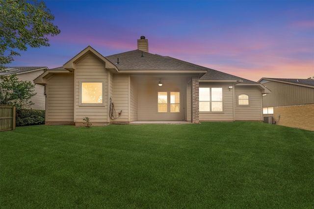 back house at dusk featuring a patio, central air condition unit, and a yard