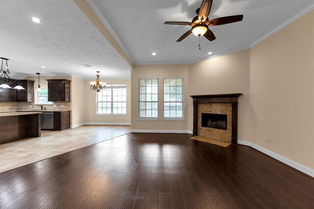 unfurnished living room featuring ornamental molding, light wood-type flooring, ceiling fan with notable chandelier, and a textured ceiling