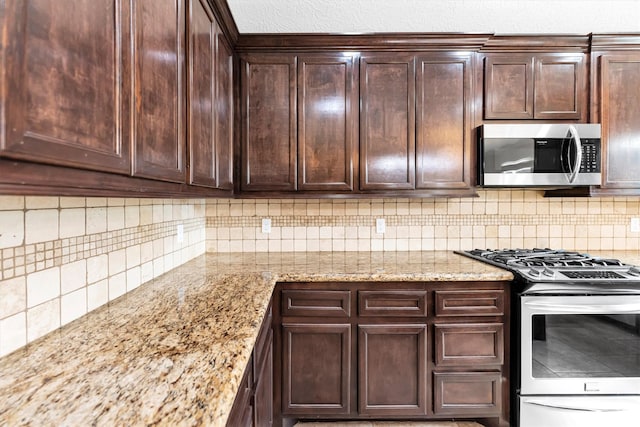 kitchen with dark brown cabinetry, decorative backsplash, stainless steel appliances, and light stone counters