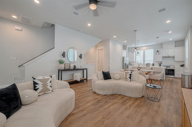 living room with ceiling fan with notable chandelier and light hardwood / wood-style flooring