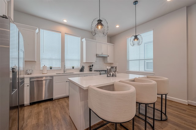 kitchen with white cabinets, light wood-type flooring, stainless steel appliances, and decorative light fixtures