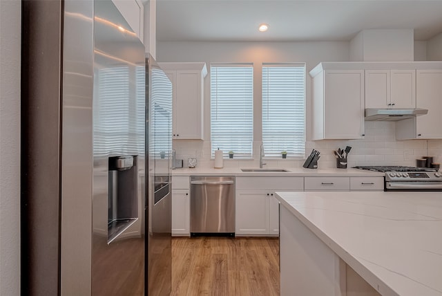 kitchen with stainless steel appliances, light hardwood / wood-style floors, sink, white cabinets, and decorative backsplash